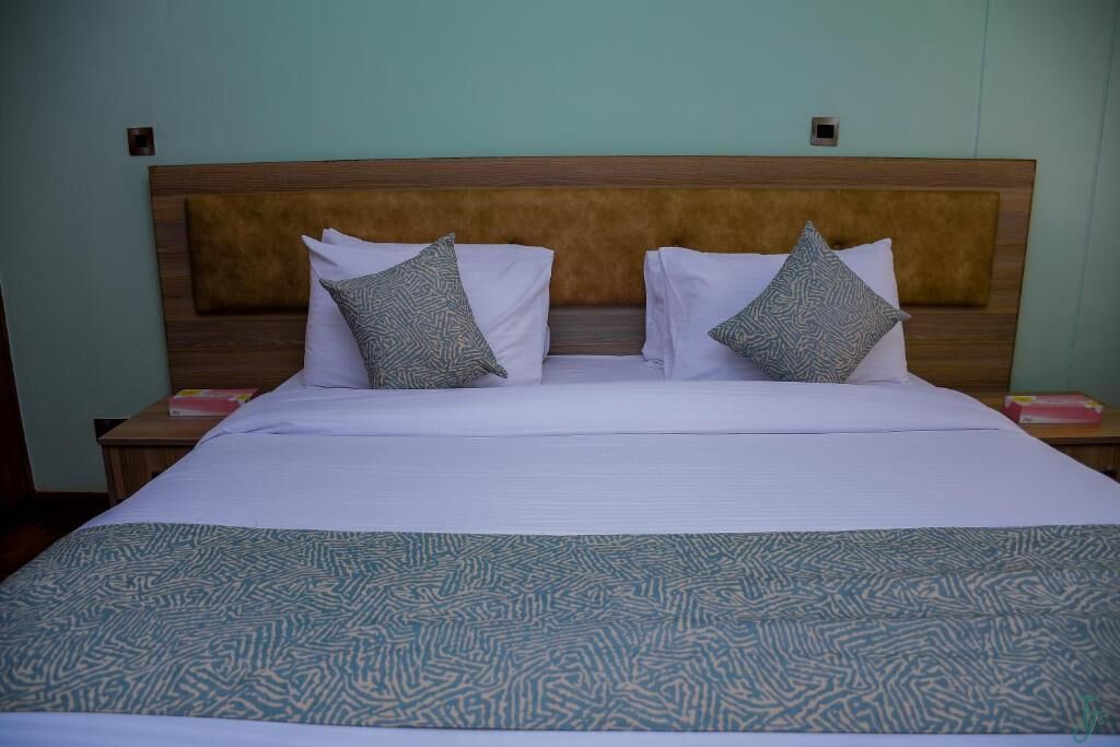 A neatly made bed with a patterned bedspread and two pillows, a wooden headboard, and a nightstand with a book and a phone.