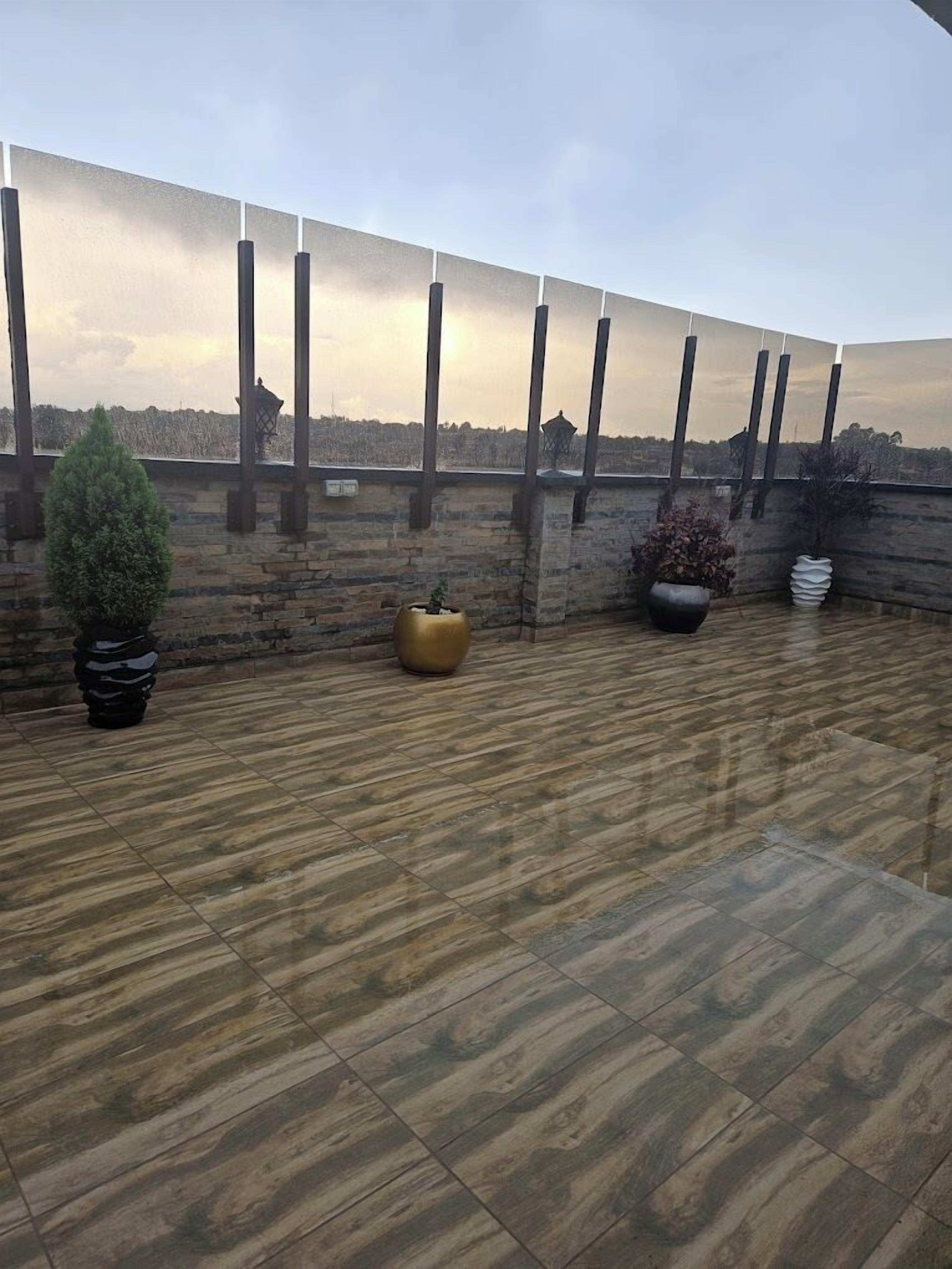 A rooftop terrace with a stone wall, potted plants, and a view of the city skyline.