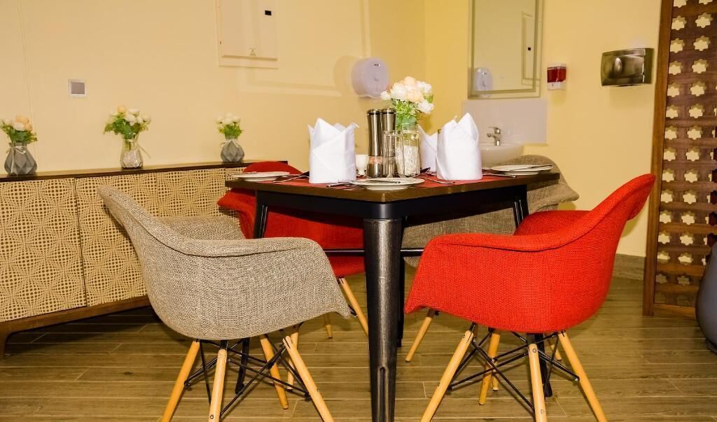 A dining area with a table set for two, surrounded by wicker chairs, and a red chair.