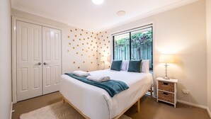A bedroom with a bed, a nightstand, a lamp, a window, and a door. - Under the Grapevines with Pool & BBQ (Dubbo)
