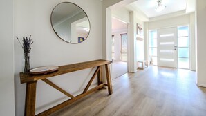 A spacious hallway with a wooden bench, a round mirror, and a vase of dried flowers. - Under the Grapevines with Pool & BBQ (Dubbo)