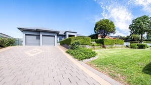 A modern residential building with a paved driveway, neatly trimmed hedges, and a well-maintained lawn. - Under the Grapevines with Pool & BBQ (Dubbo)