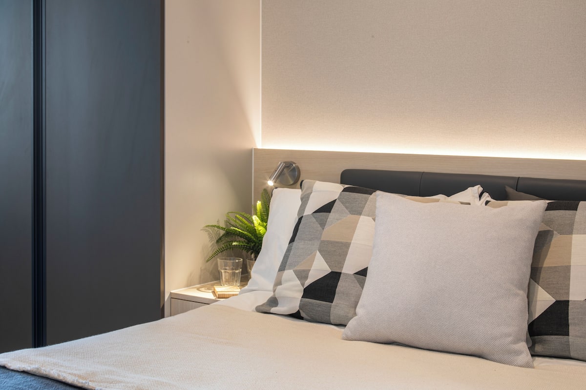 A neatly made bed with a geometric patterned pillow, a bedside lamp, and a small potted plant on a nightstand.