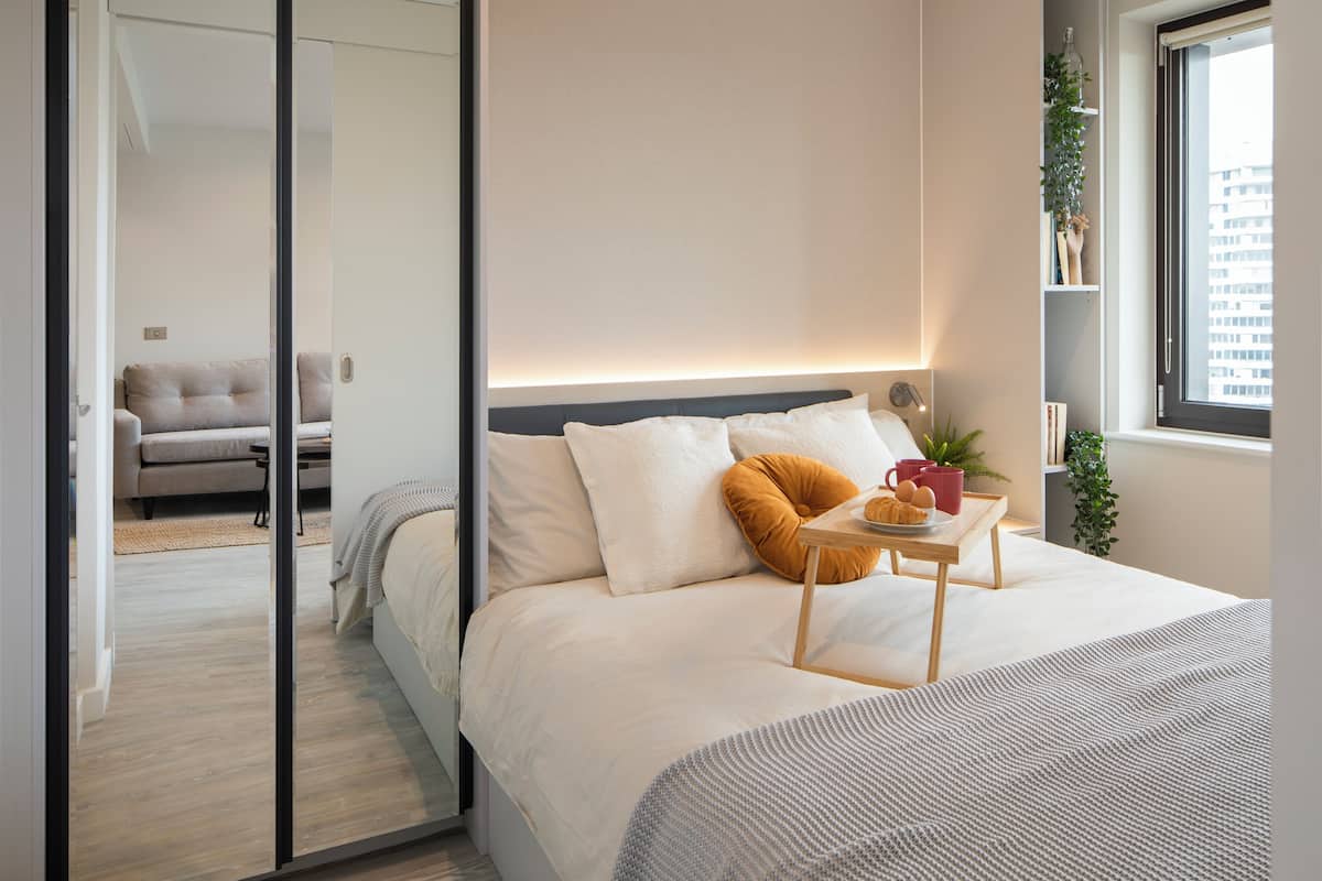 A modern bedroom with a bed, bedside table, and a window with a city view.