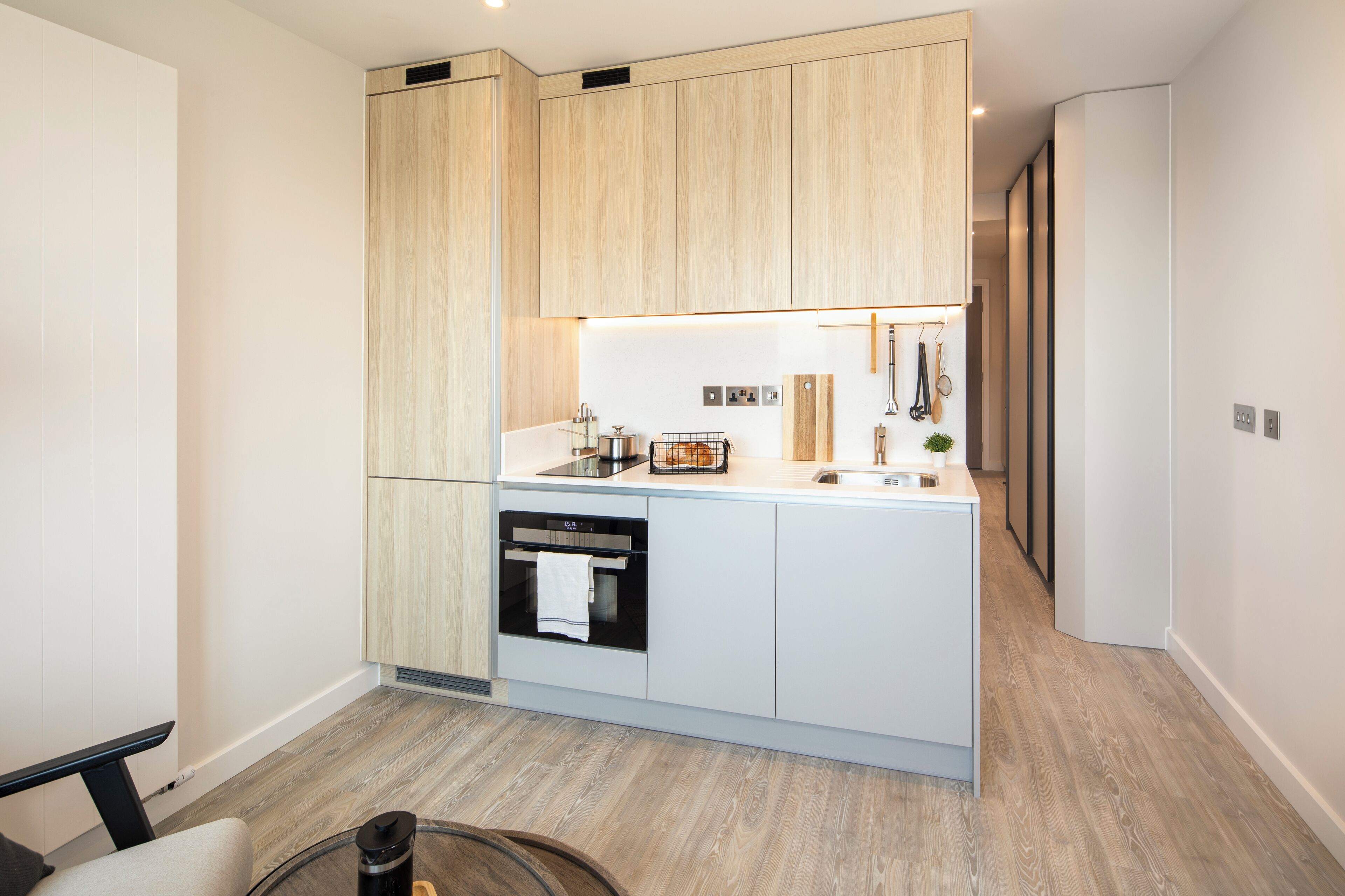Una cocina moderna con armarios de madera, horno empotrado y encimera con distintos utensilios de cocina.