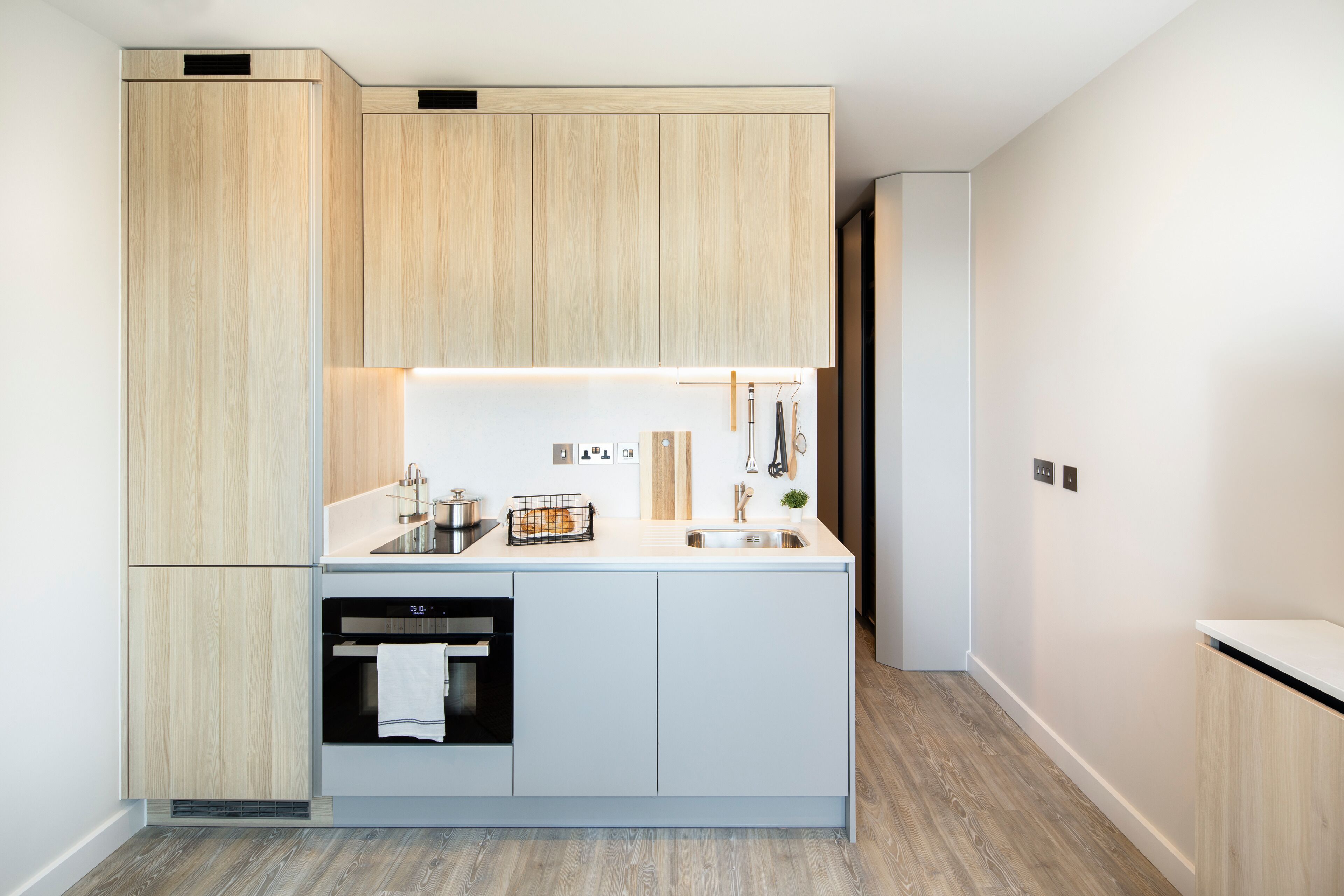 Una cocina moderna con armarios de madera clara, horno empotrado y encimera con un fregadero y diversos utensilios de cocina.