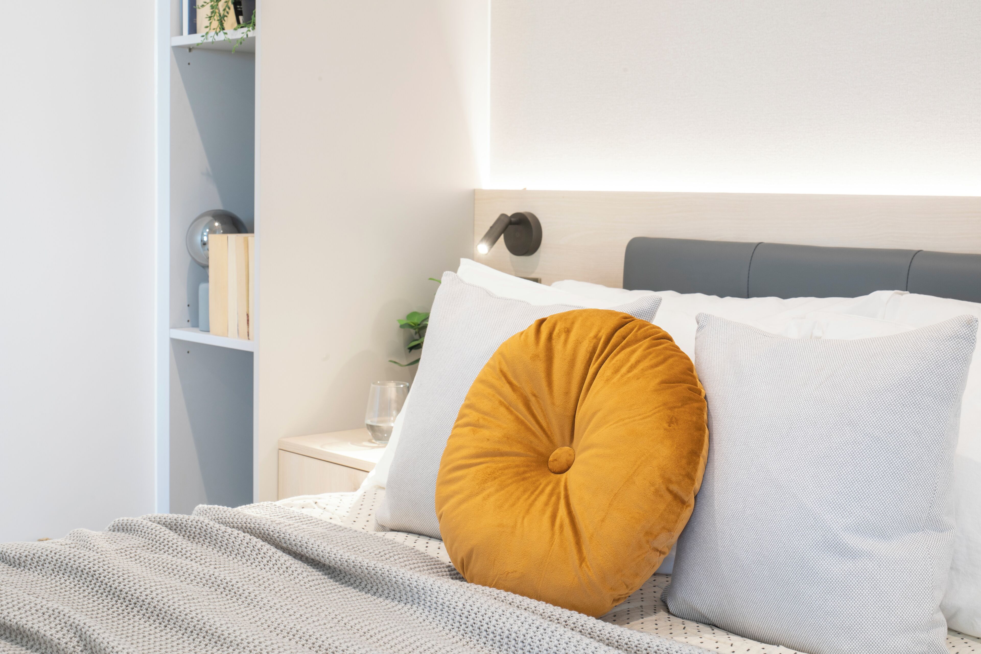 Een net opgemaakt bed met een gestreept kussen en een rond, mosterdkleurig kussen.