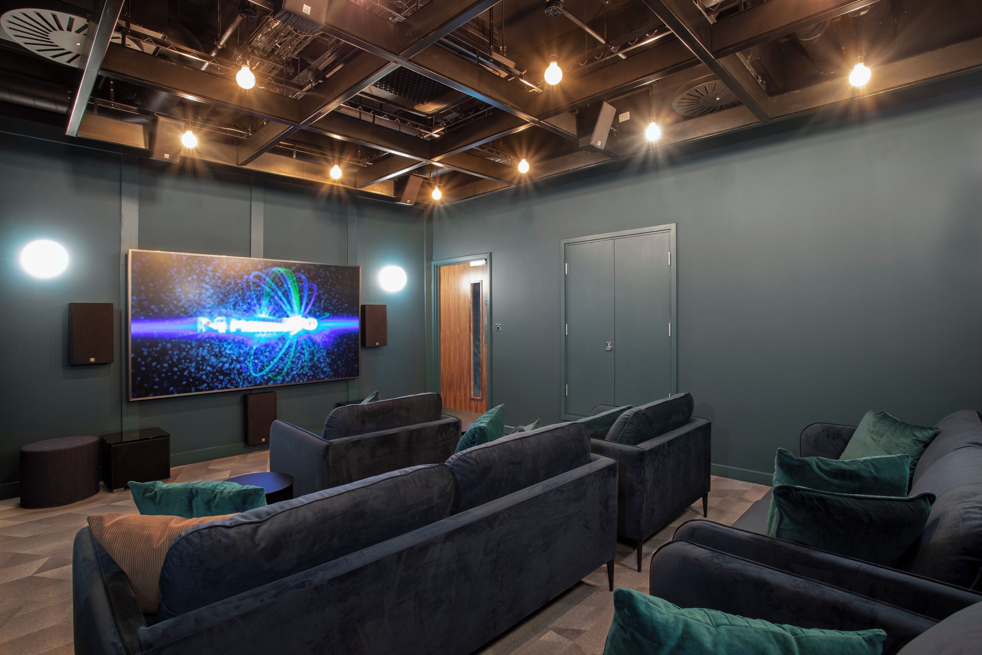 A modern cinema room with dark seating, a large screen, and ambient lighting.