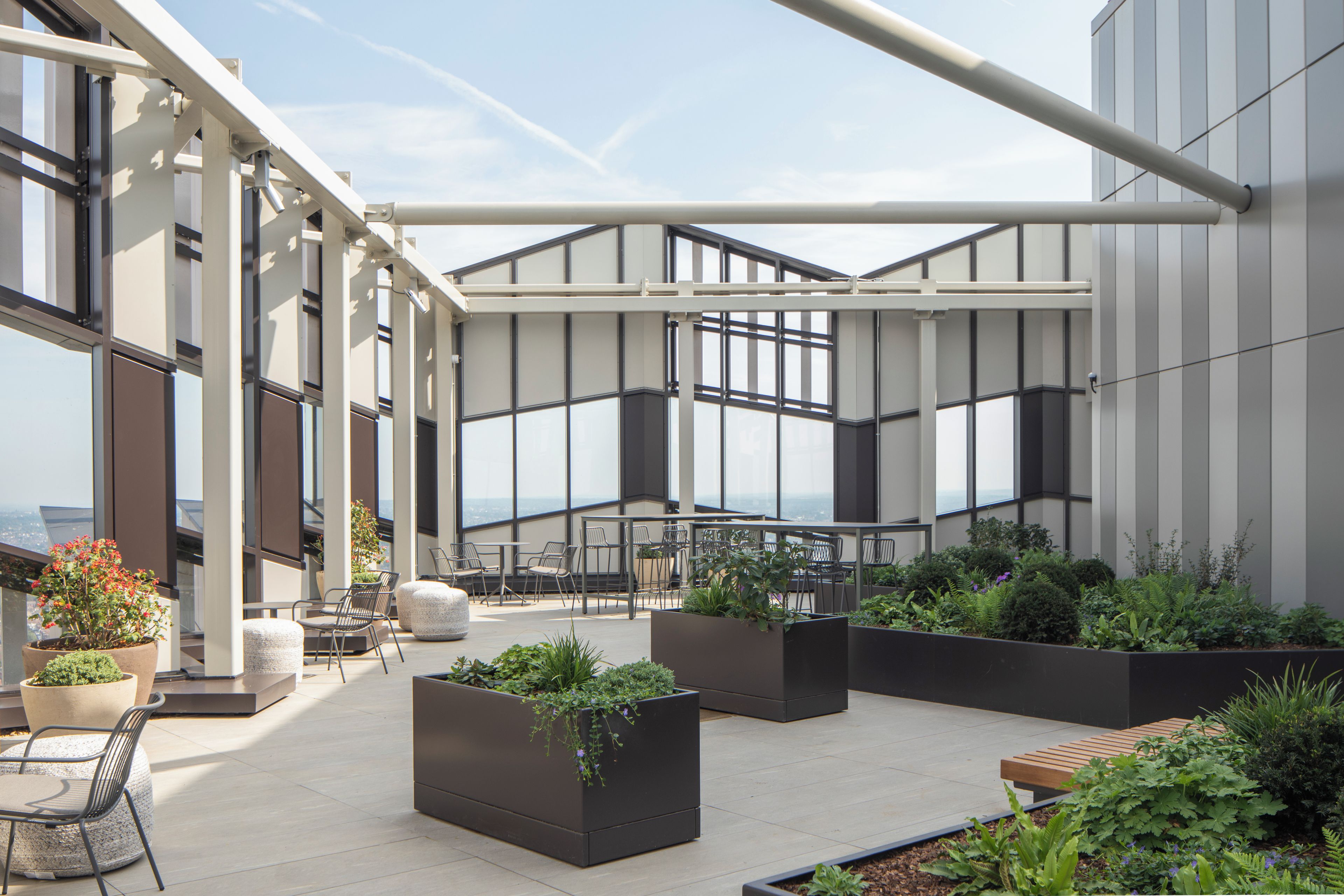 A rooftop terrace with outdoor seating, planters, and large windows offering views.
