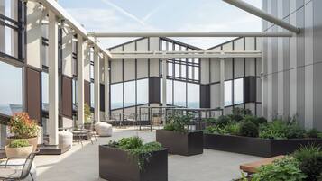 A rooftop terrace with outdoor seating, planters, and large windows offering views.