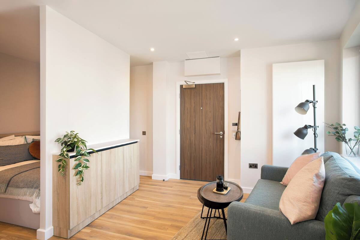 A modern living room with a sofa, a small round table, and a kitchen area with a wooden cabinet and a plant.