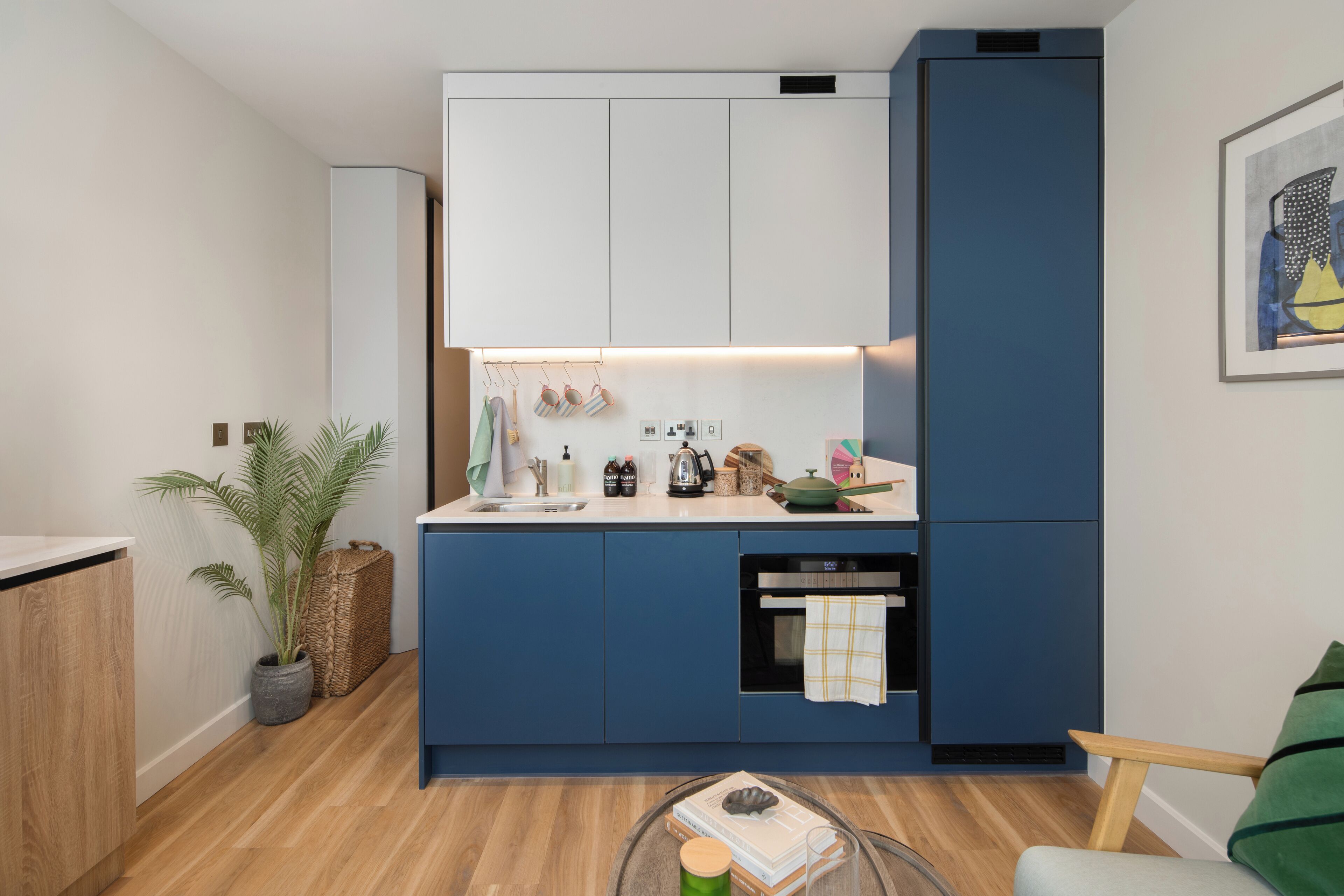 Eine kleine Küche mit weißen Oberschränken, einem blauen Unterschrank und einem eingebauten Backofen.