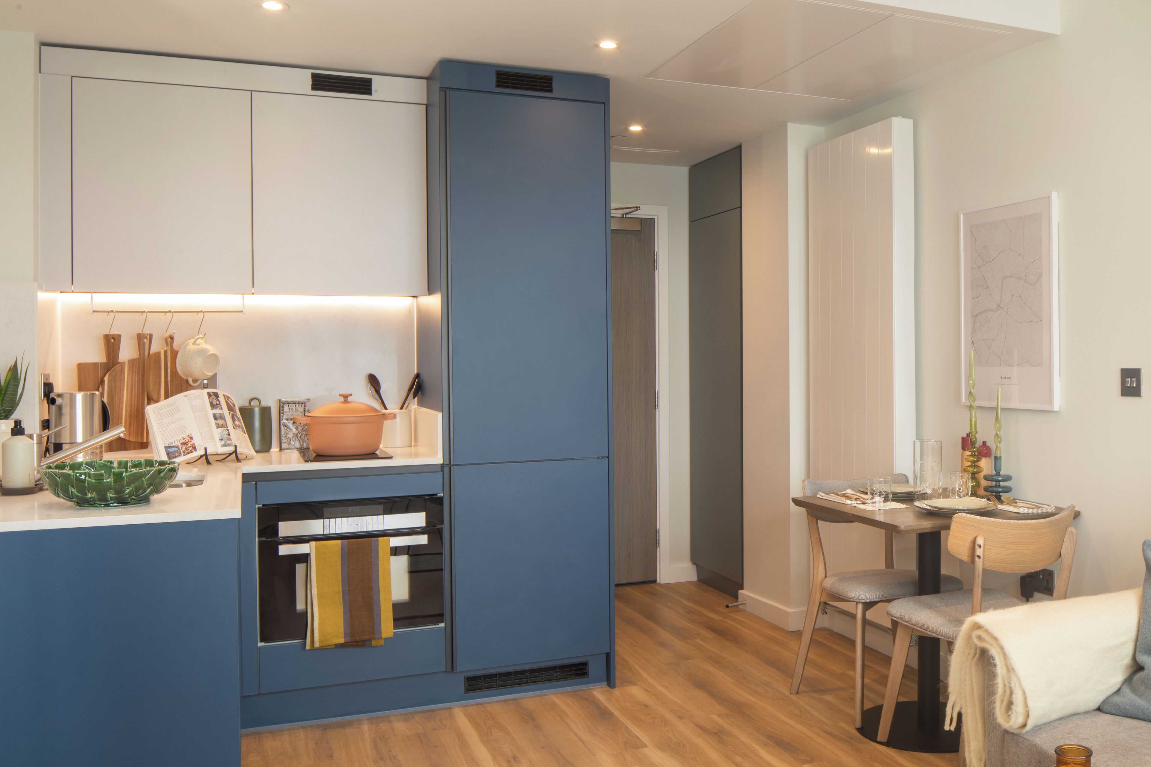 A modern kitchen with a blue cabinet, a dining area with a table and chairs, and a cozy seating area with a sofa.