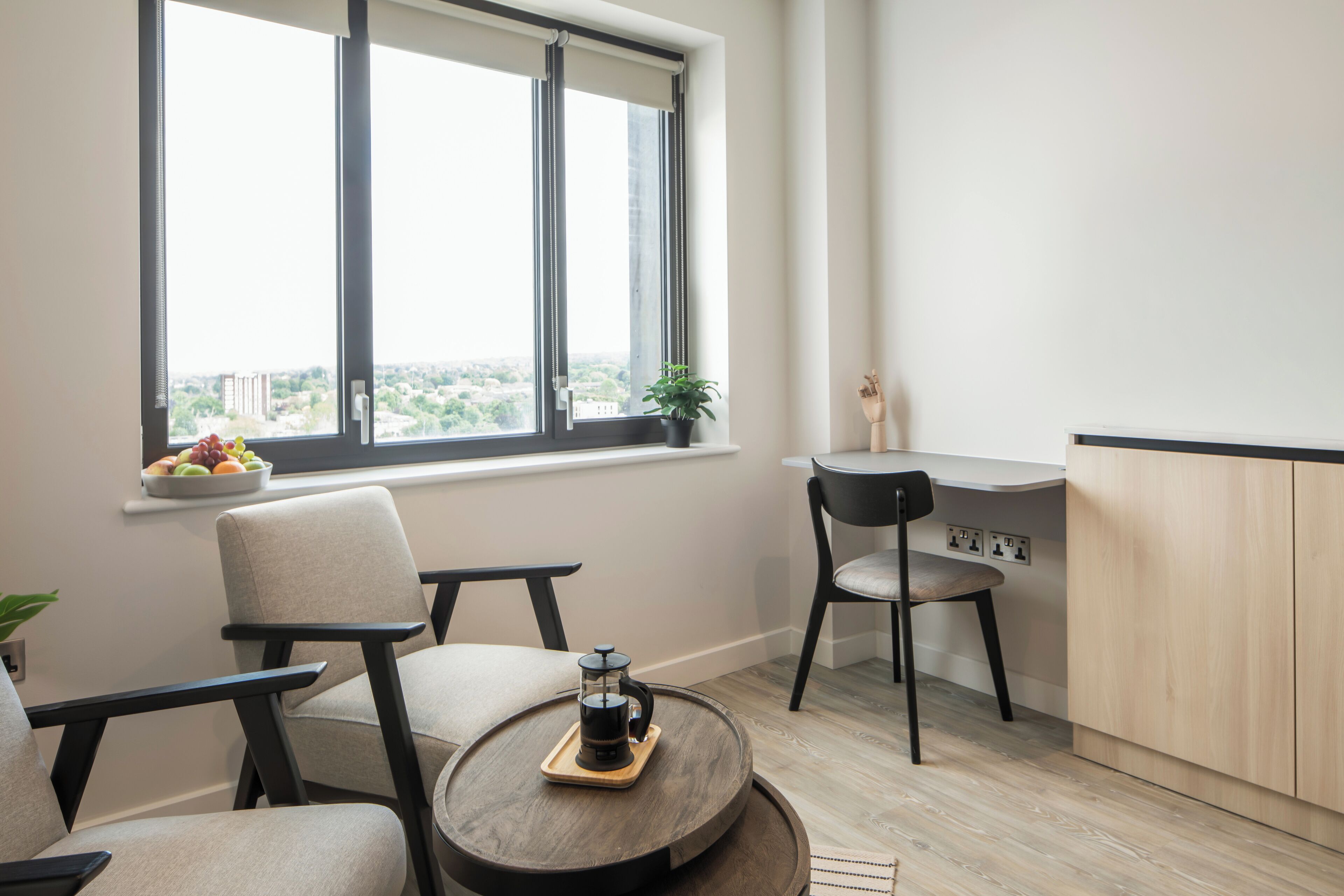 Una sala de estar moderna con una mesa redonda, dos sillas, una mesita con una planta y vistas amplias a través de grandes ventanales.