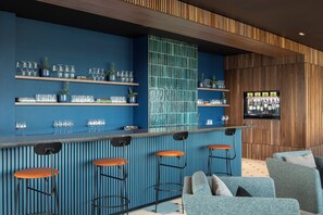 A bar area with blue walls, wooden paneling, and bar stools. Shelves hold glasses and small plants. - Staycozy Studio Apartments in Croydon (Croydon)
