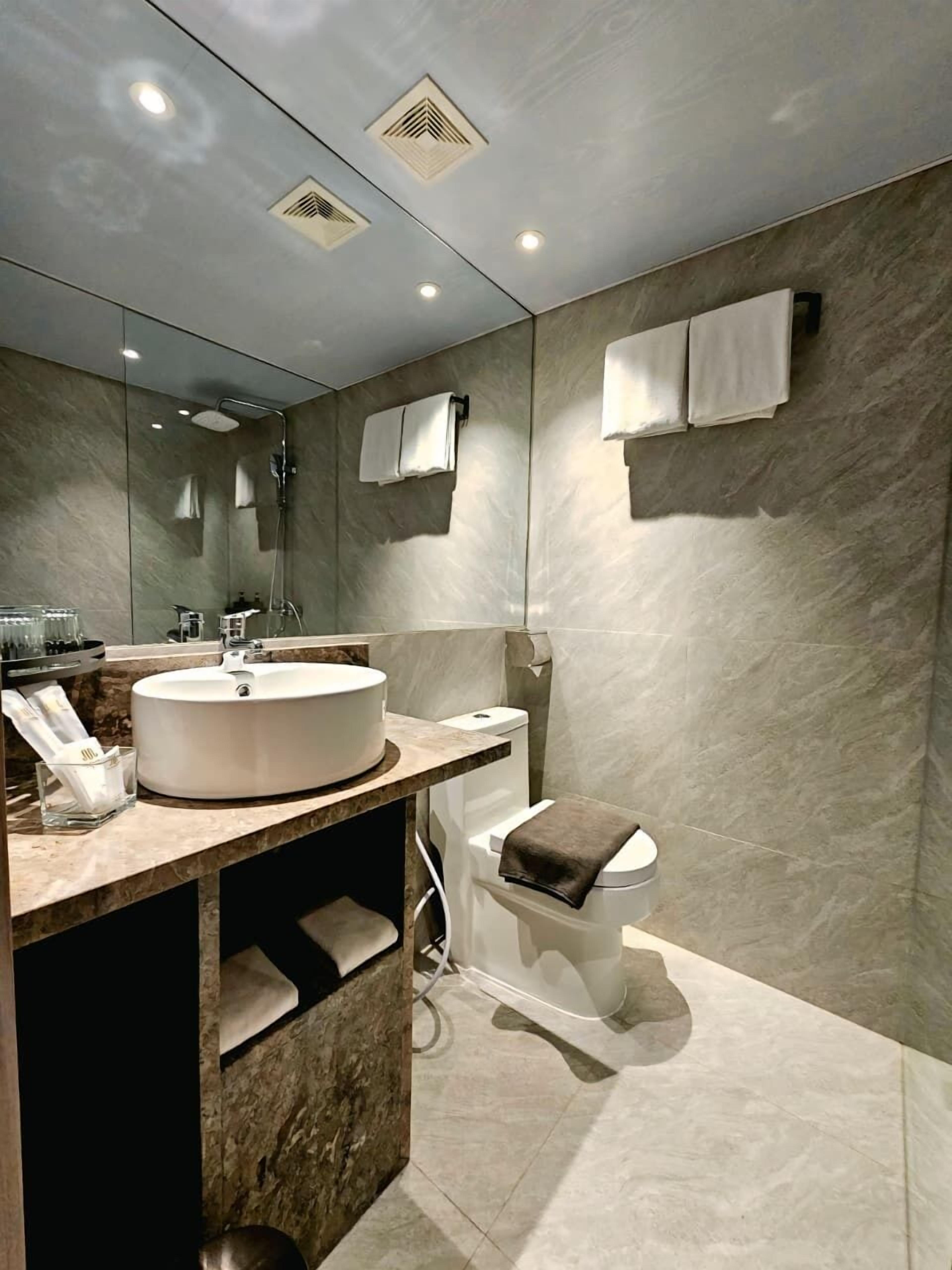A modern bathroom with a large mirror, a round sink, a toilet, and a shower.