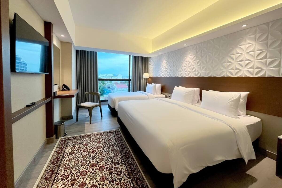Een hotelkamer met een groot bed, een bureau, een stoel en een aan de muur bevestigde televisie.