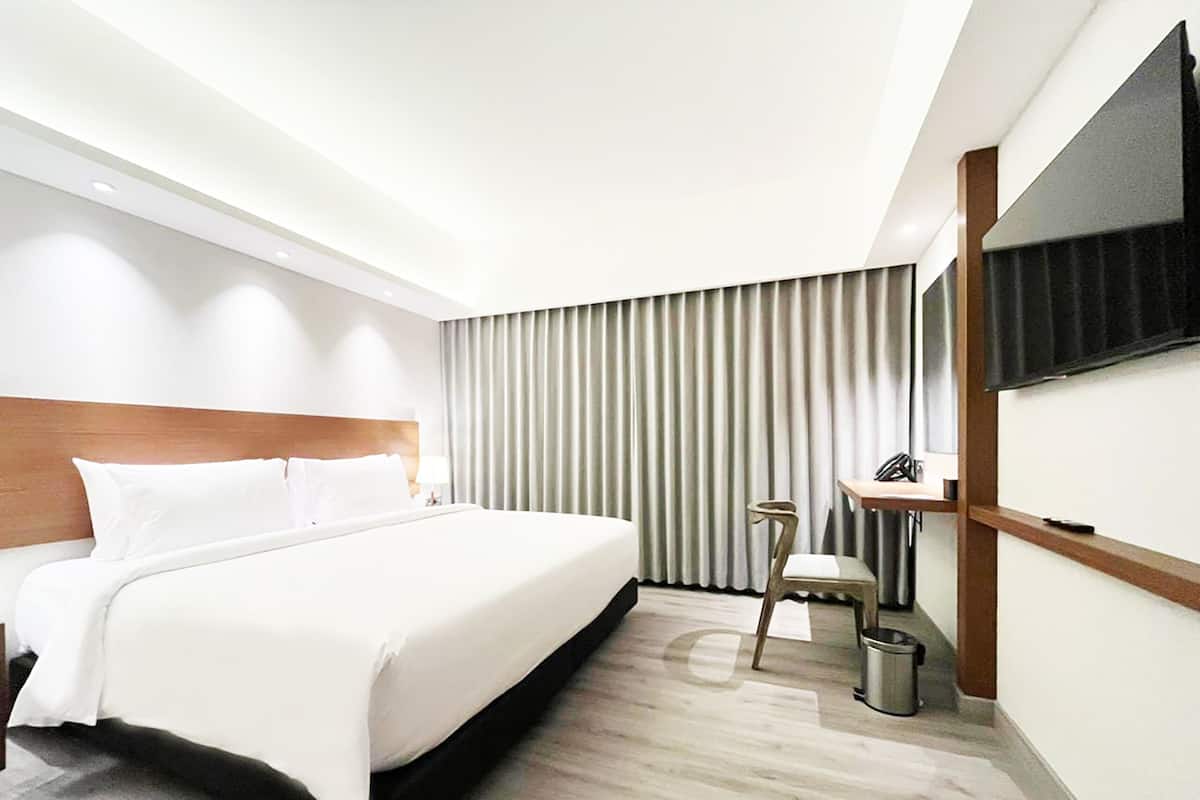Een moderne hotelkamer met een groot bed, een bureau, een stoel, een aan de muur bevestigde televisie en een raam met gordijnen.