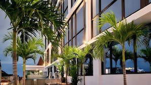 An outdoor seating area with lounge chairs and tables, surrounded by tall palm trees, and overlooking a body of water. - The Jogja Hotel & Conference Center - Malioboro (Yogyakarta)