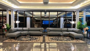 A modern lobby with a grey sectional sofa, a reflective floor, and a ceiling with wooden panels and recessed lighting. - The Jogja Hotel & Conference Center - Malioboro (Yogyakarta)