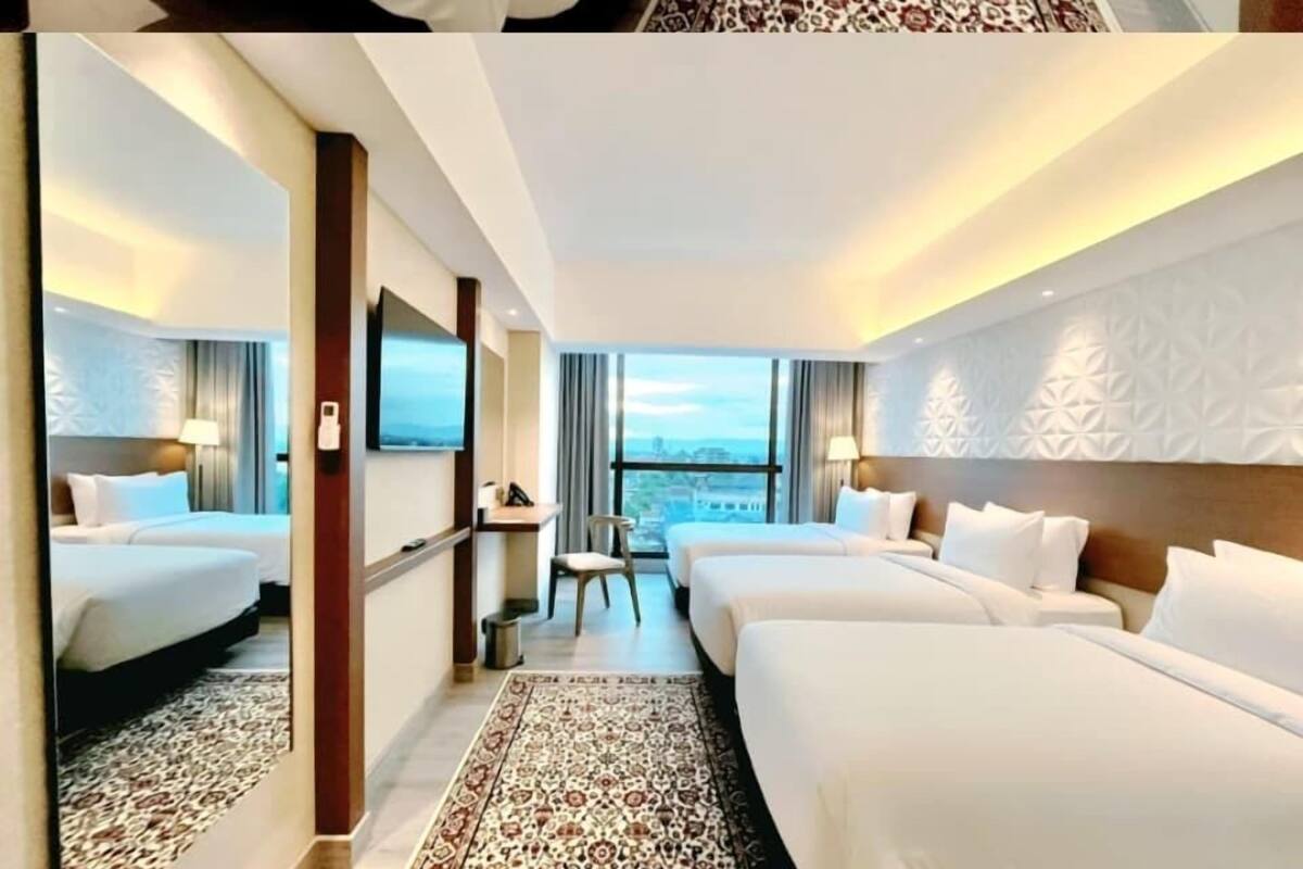 Een hotelkamer met twee bedden, een bureau, een stoel en een groot raam met uitzicht op de stad.
