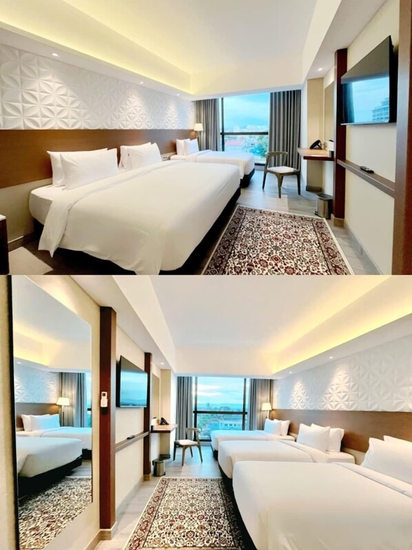 A hotel room with two beds, a desk, a chair, and a large window with a city view. - The Jogja Hotel & Conference Center - Malioboro (Yogyakarta)