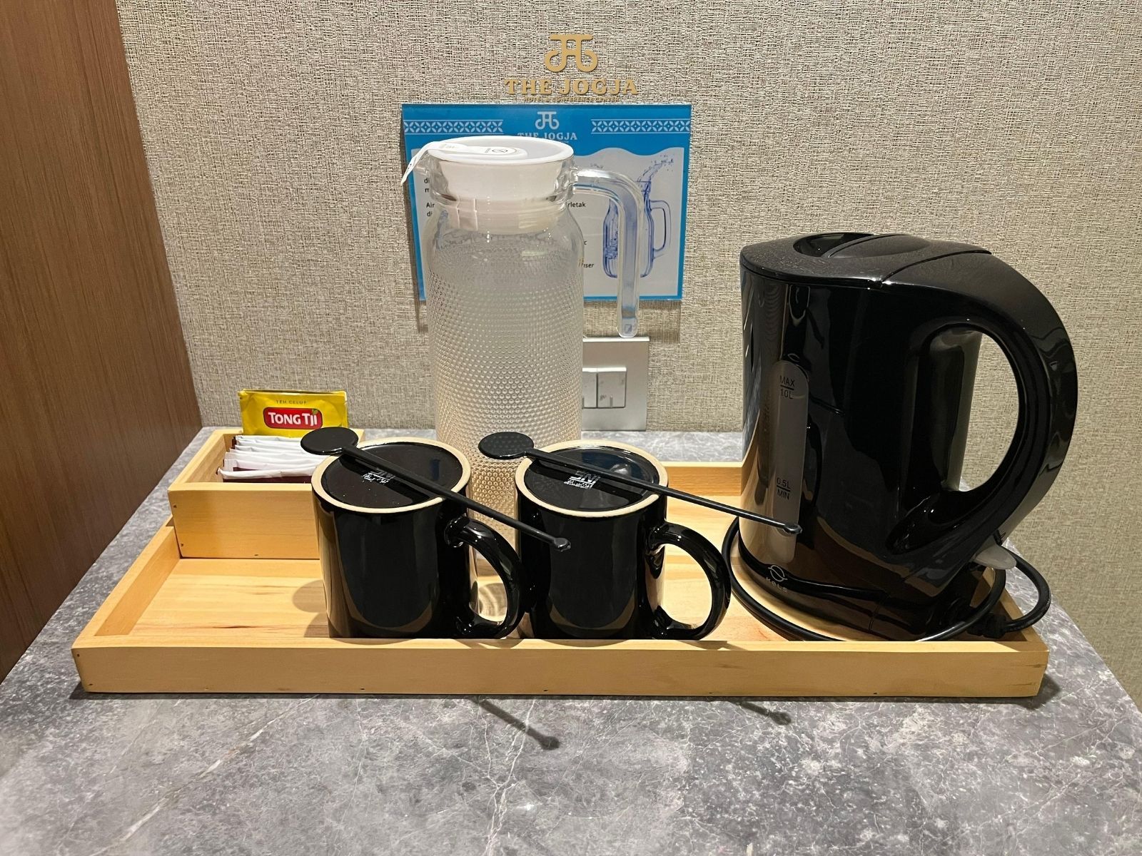 A coffee station with a kettle, two cups, a tray, and a box of TONGTJI tea.