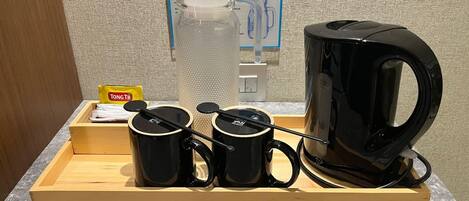 A coffee station with a kettle, two cups, a tray, and a box of TONGTJI tea.