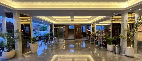 A hotel lobby with a polished marble floor, a reception desk, and a view of the outside.