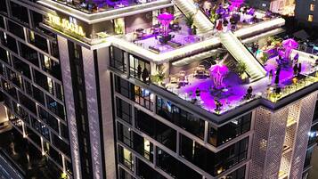 Un hotel de varios pisos con terraza en la azotea, mobiliario exterior y un escenario.