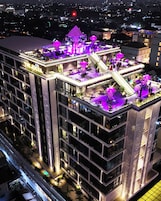 Un hôtel à plusieurs étages doté d’une terrasse sur le toit, comprenant un espace extérieur avec des sièges et une scène.