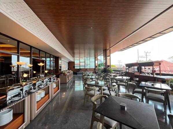 A spacious restaurant with a long counter, multiple tables, and a view of the cityscape. - The Jogja Hotel & Conference Center - Malioboro (Yogyakarta)