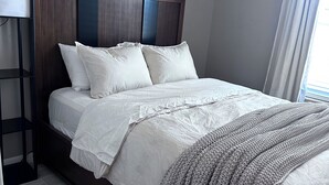 Ein modernes Schlafzimmer mit einem Holzkopfteil, einem Nachttisch und einem großen Fenster mit Vorhängen.