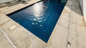 A rooftop pool with clear blue water, surrounded by lounge chairs and a modern building with a grid-like facade. - Modern Flat in Gonzaga, just a block from the beach. (Santos)
