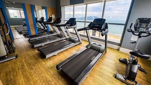 A gym with multiple treadmills, exercise bikes, and a large window offering a view of the city. - Modern Flat in Gonzaga, just a block from the beach. (Santos)