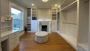 A walk-in closet with wooden flooring, built-in drawers, shelves, and a fireplace.