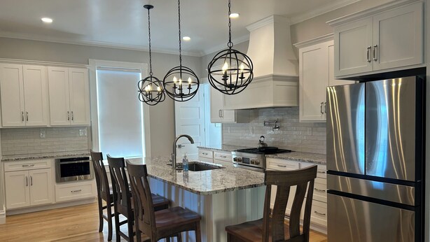 A modern kitchen with white cabinets, a stainless steel refrigerator, a granite countertop, and a central island with bar stools.