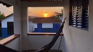A hammock in a balcony with a view of a sunset over houses. - Fazenda Brasileiro (Passos)