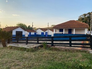 A row of white buildings with blue trim and tiled roofs, separated by a black fence. - Fazenda Brasileiro (Passos)