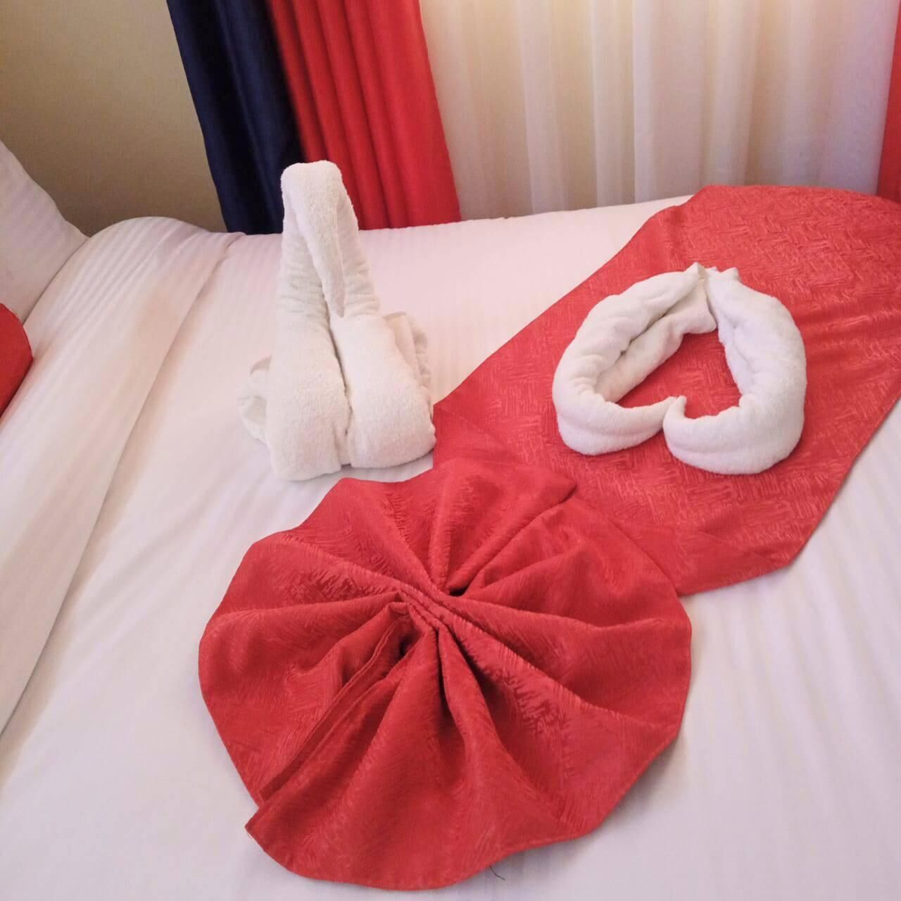 A neatly made bed with a red towel and a white towel folded on it.