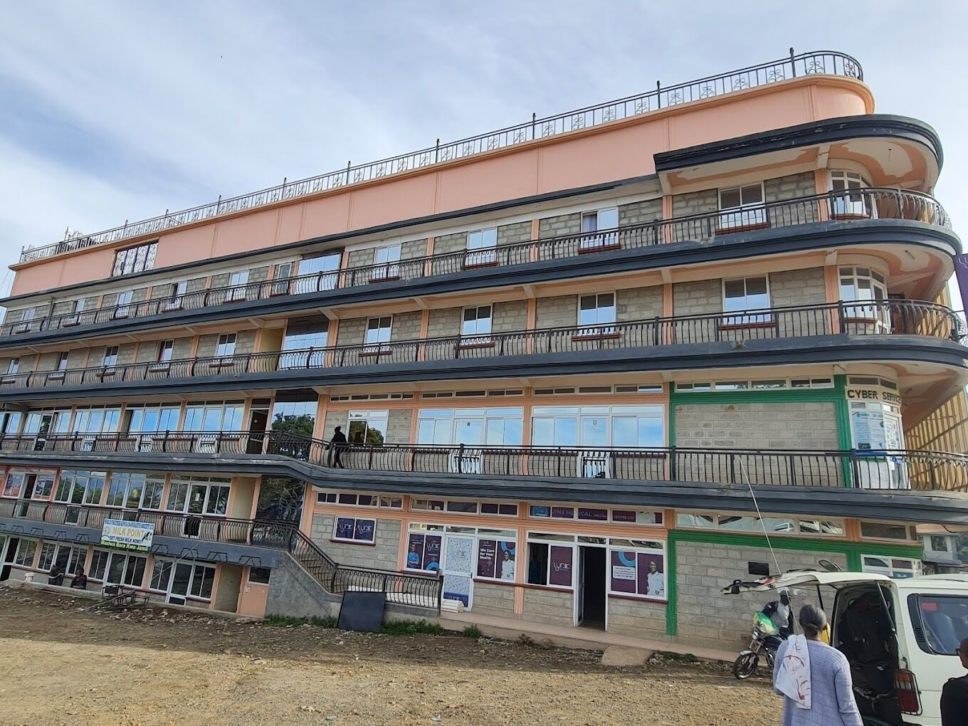 A multi-story building with balconies, a ground-level shop, and a sign for a cyber cafe.