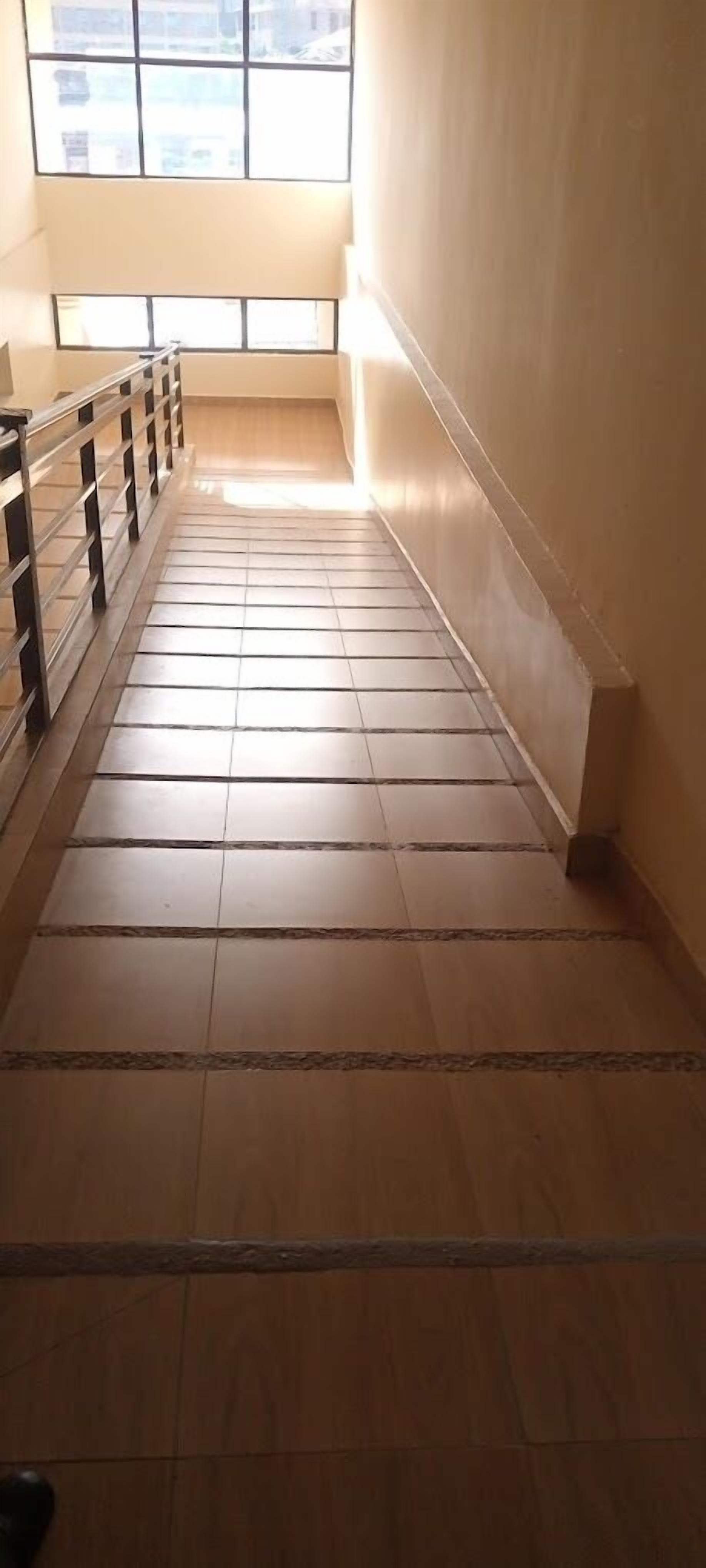 Uma escadaria de azulejos com corrimão de metal, conduzindo a uma área iluminada com janelas.