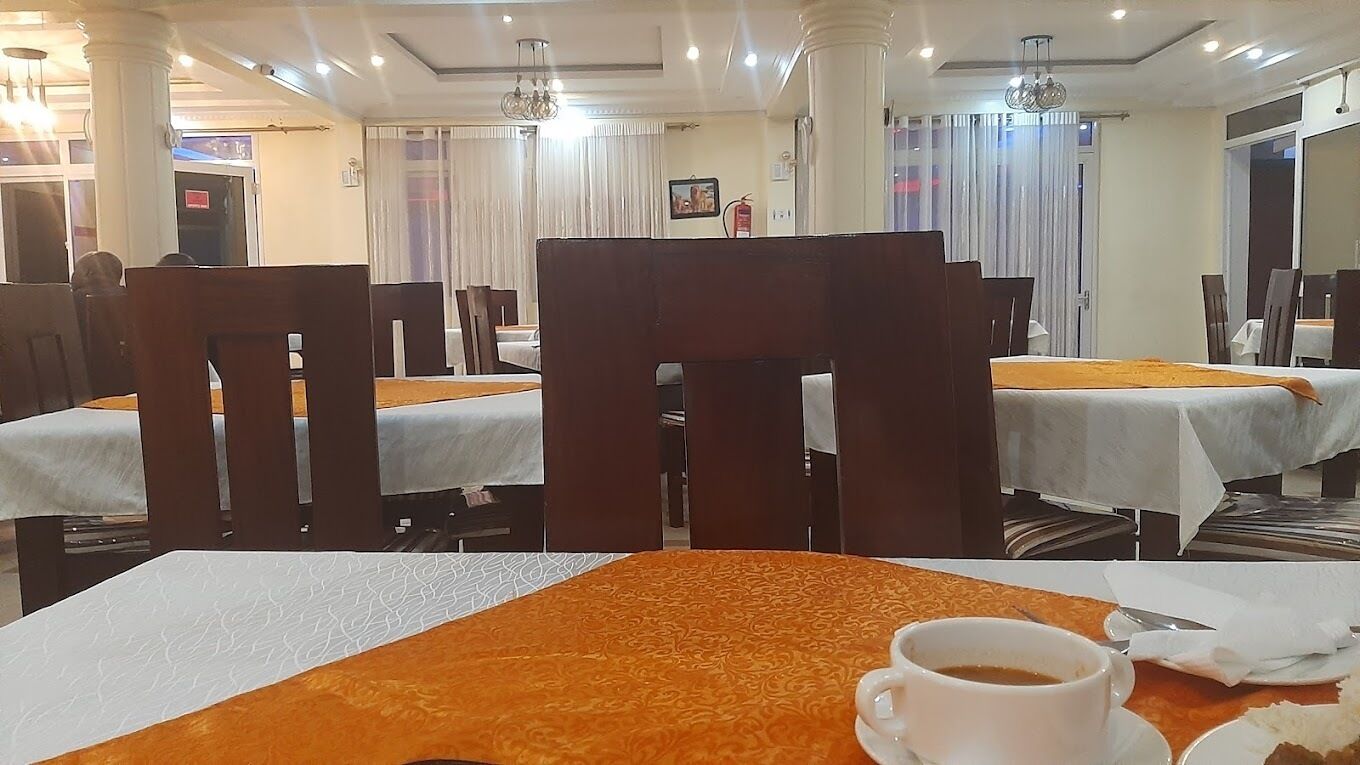 A hotel dining area with tables covered in white tablecloths, wooden chairs, and orange table runners.
