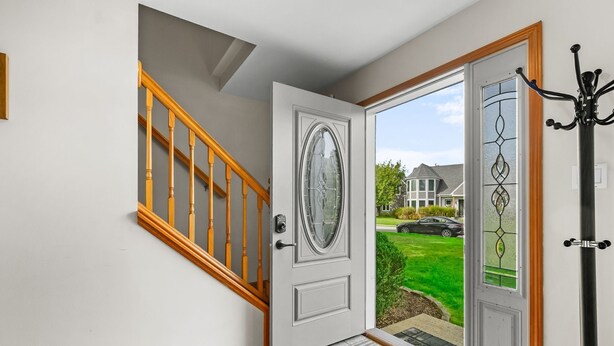 Un hall d’entrée moderne avec un escalier en bois, une porte en verre ornée d’un motif décoratif et une vue sur un quartier résidentiel.