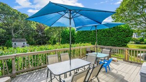 Une terrasse extérieure couverte, dotée d’une table et de chaises, entourée d’une terrasse en bois et d’une clôture.