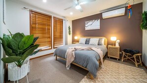 A bedroom with a bed, bedside tables, a ceiling fan, and a large window with blinds. - Amazon at Seacombe Gardens—Vibrant Family Oasis (Seacombe Gardens)