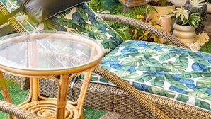 A wicker lounge chair with a glass table, surrounded by various potted plants and a small decorative fountain. - Amazon at Seacombe Gardens—Vibrant Family Oasis (Seacombe Gardens)
