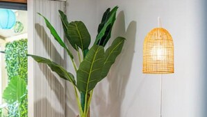 A living room with a beige sofa, a large green plant, a tall floor lamp, and a small white side table with a remote control. - Amazon at Seacombe Gardens—Vibrant Family Oasis (Seacombe Gardens)