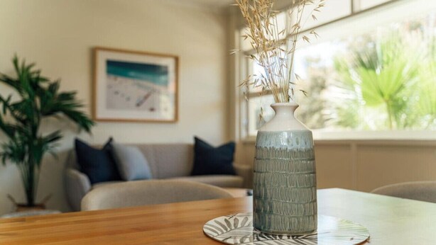 Une table en bois, sur laquelle se trouve un vase contenant des plantes séchées, et un tableau encadré accroché au mur.