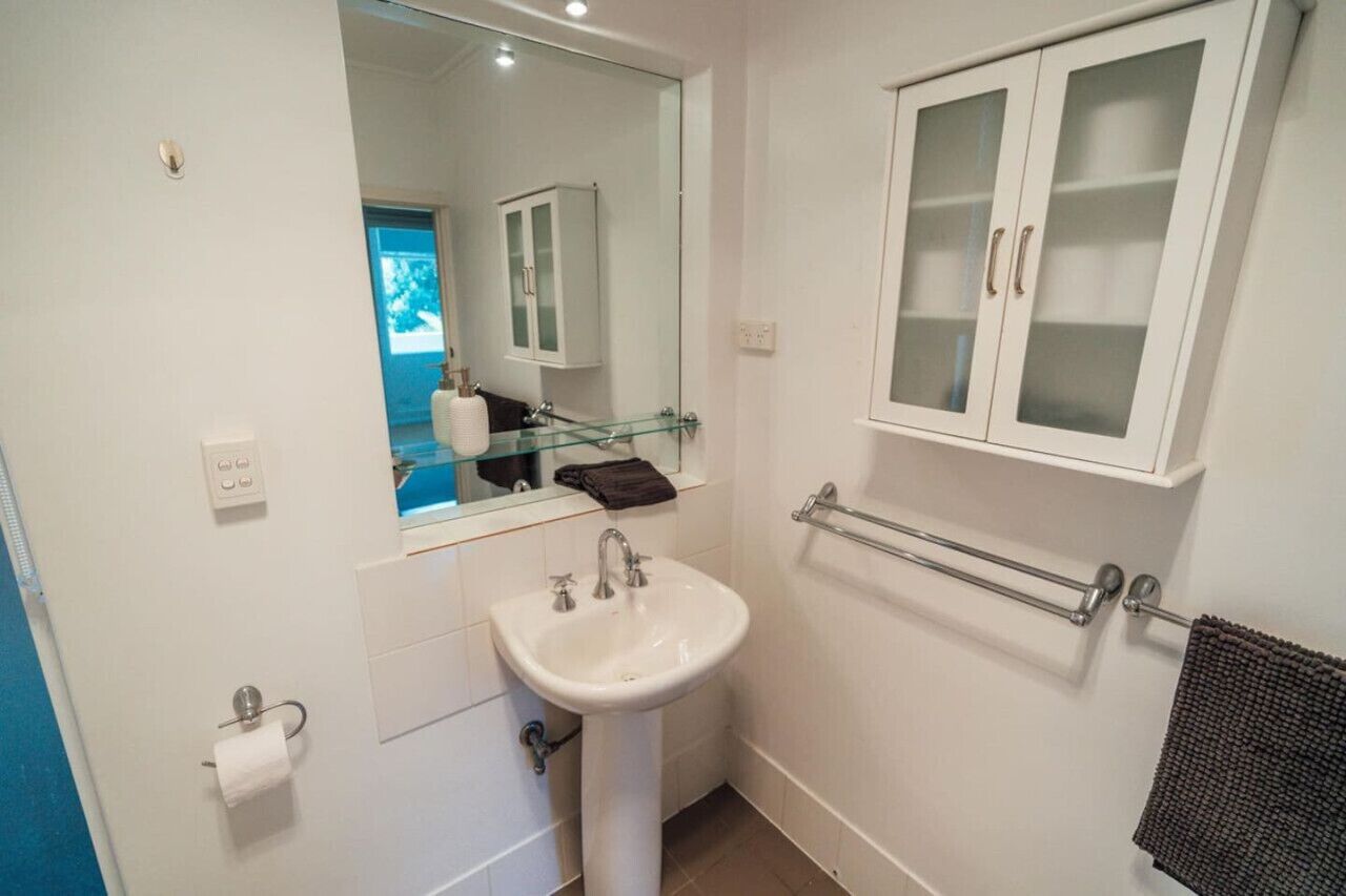 Une salle de bain avec un lavabo blanc, une cabine de douche en verre, un meuble blanc avec des portes en verre dépoli et un porte-serviettes.